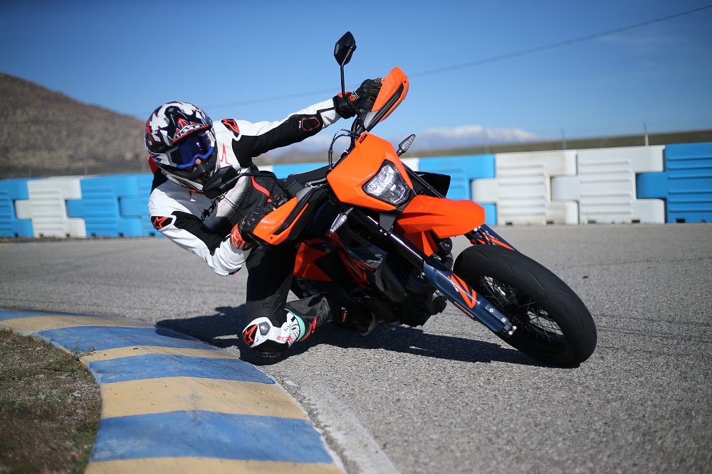 view of Dylan leaned over at an extreme angle on the SMC R at the track, coming toward the camera