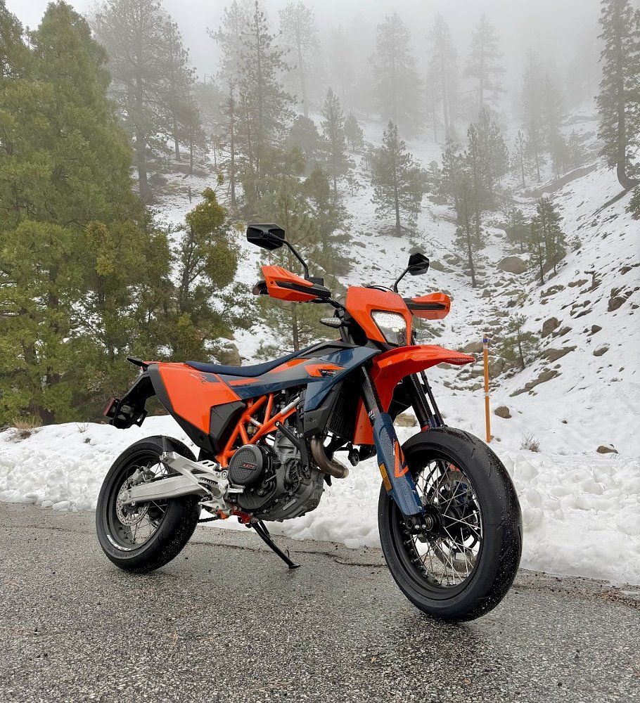the KTM 690 SMC R parked alongside a mountain road, a snow-covered hillside behind it