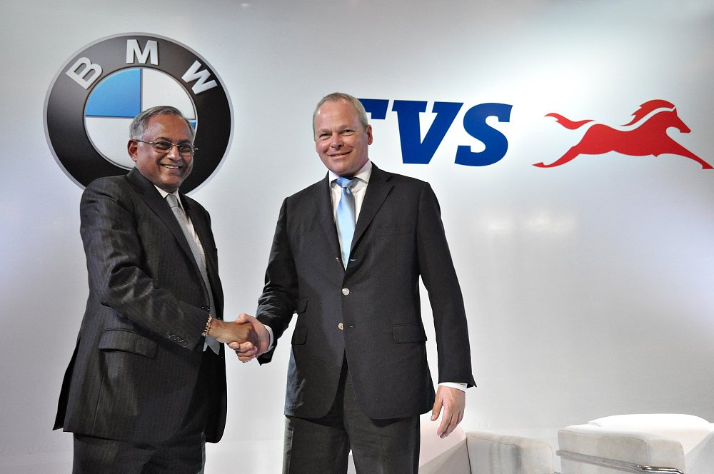 the two executives shaking hands in front of BMW and TVS logos on a large sign