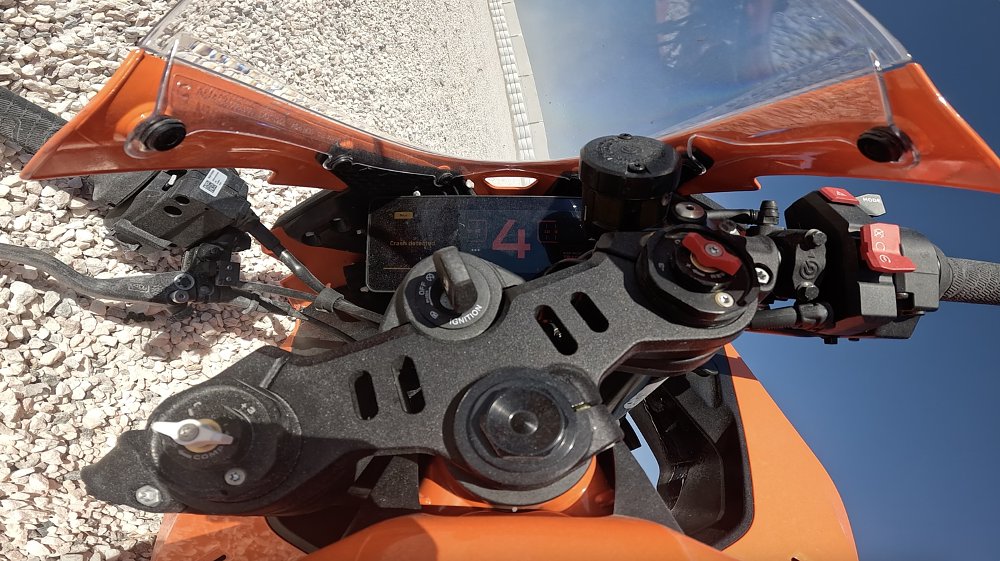 Onboard camera image from a motorcycle, showing the bike stopped on its side in a gravel trap at the Seville Circuit.