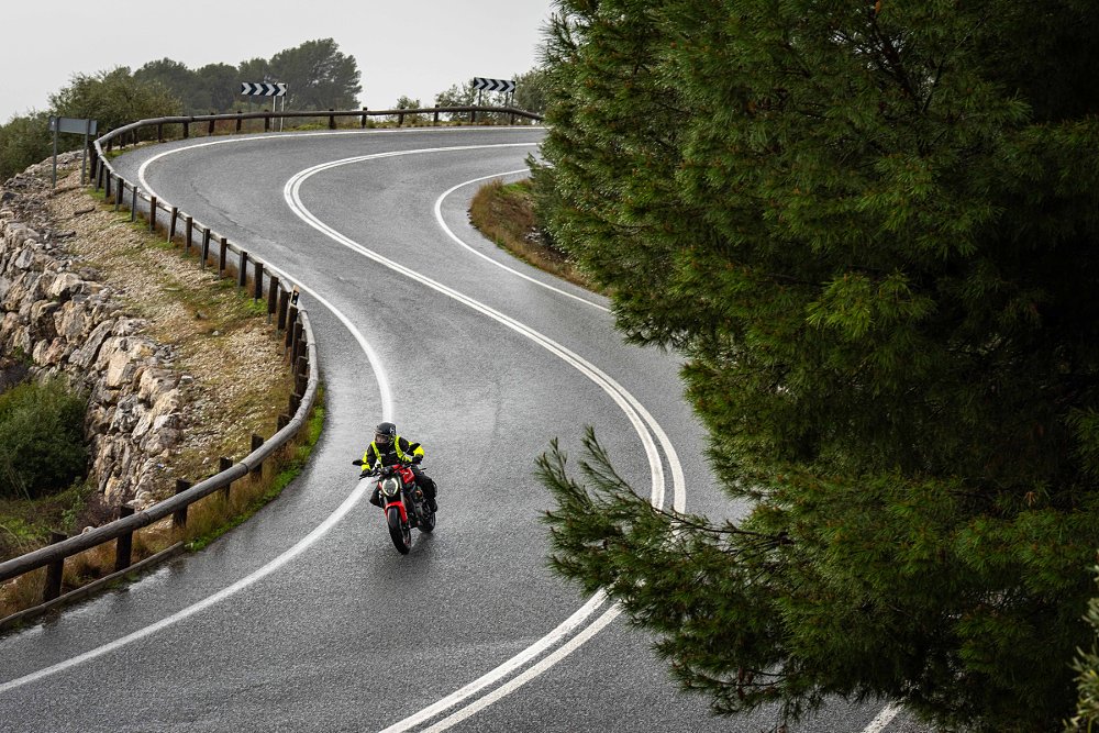 long view of the rider on the Ducati Monster descending a curving road on a hillside in light rain