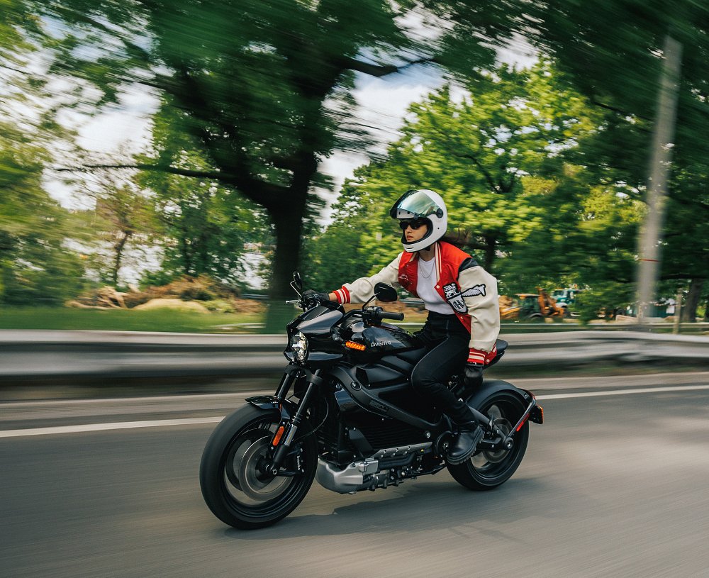 woman riding a LiveWire ONE motorcycle on a city street by a park with trees