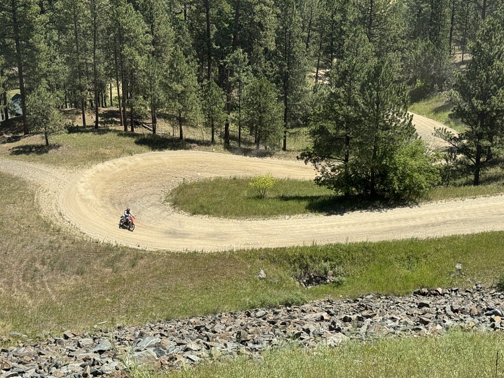 2026 KTM 690 Enduro R riding through a hairpin turn on a pale, gravel road in a forest.