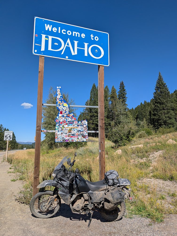 the KLR650 parked under a 'welcome to Idaho' sign