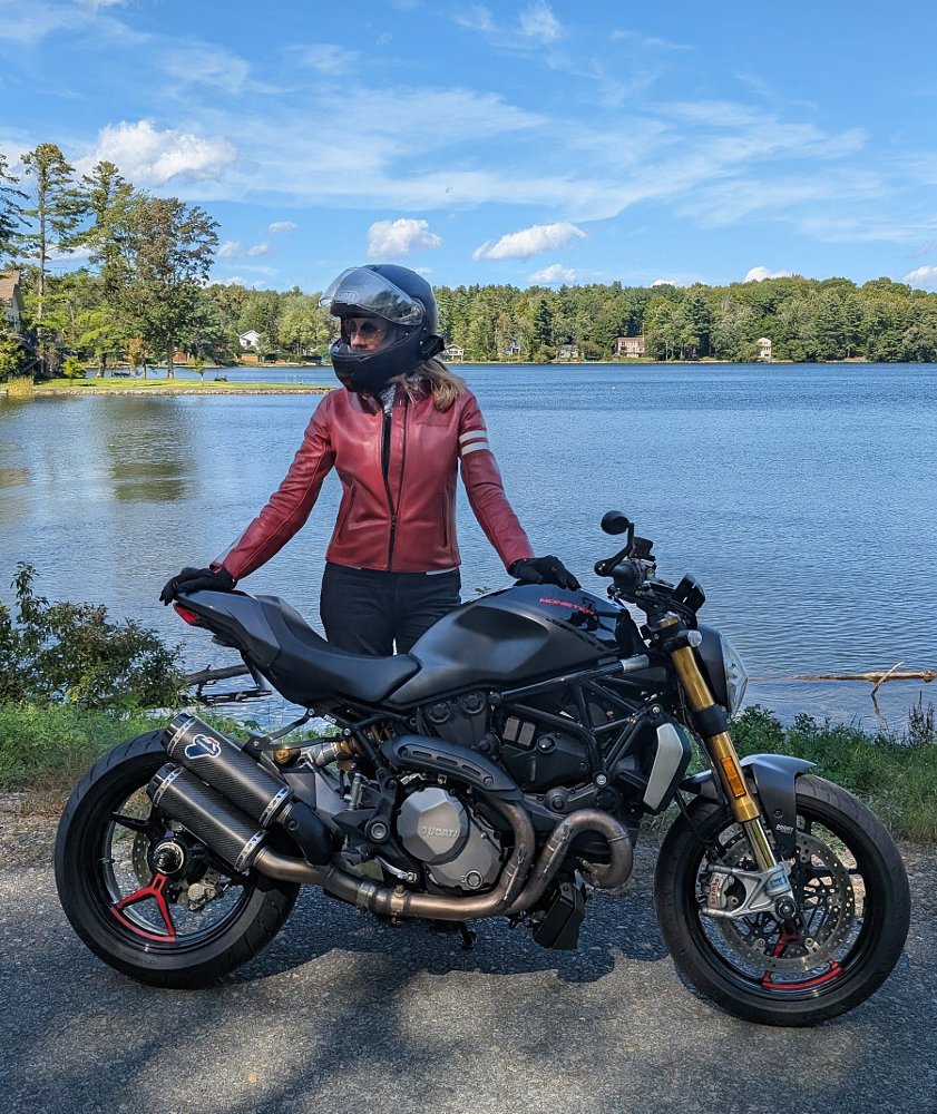 the author in a rust-colored leather jacket and black helmet beside her black Monster 1200S in front of a lake