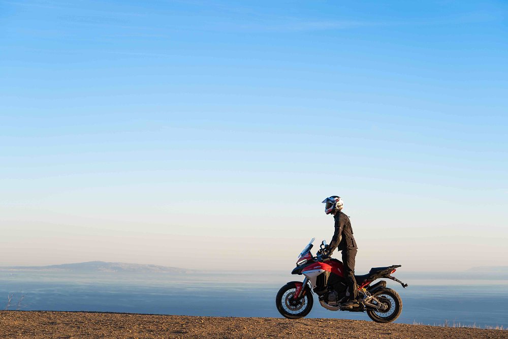 Ducati Multistrada V4 riding along a dirt trail with ocean in the background