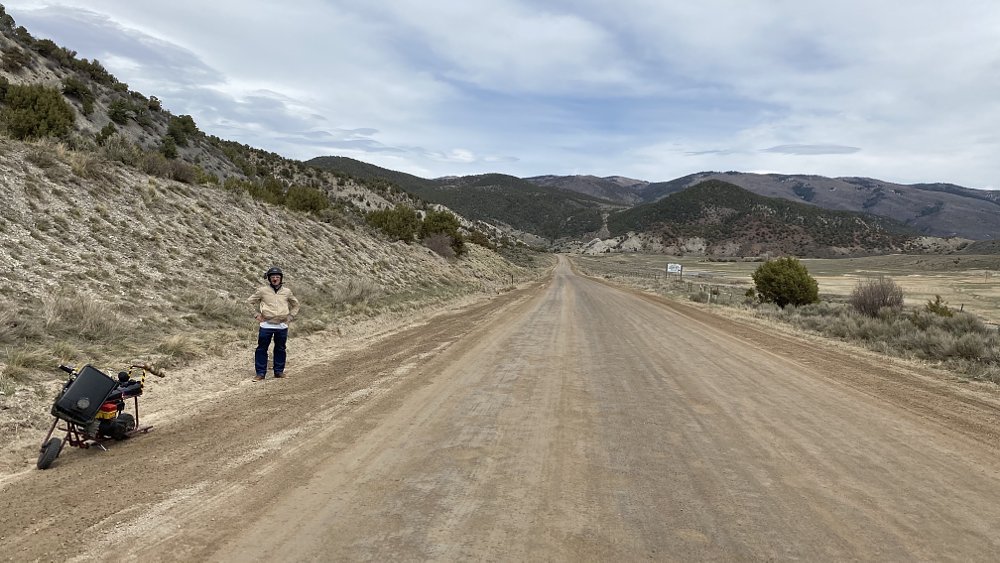 Ari standing on the side of a gravel road next to the Dumb and Dumber mini bike