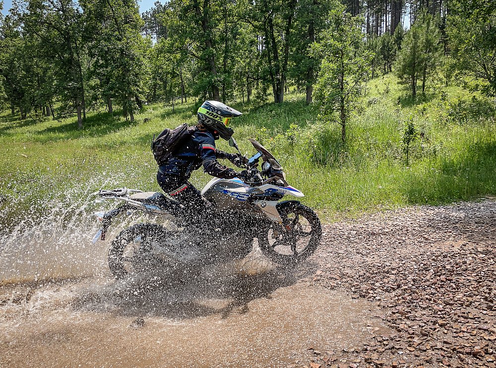 Female rider rides through a big puddle with a splash on the off-road trail on the bmw g 310 gs