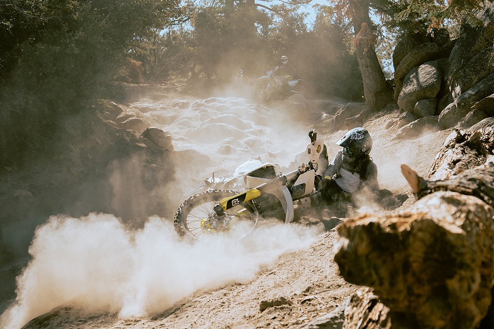 A female rider crashes on her motorcycle on the dirt trail in a giant plume of dust