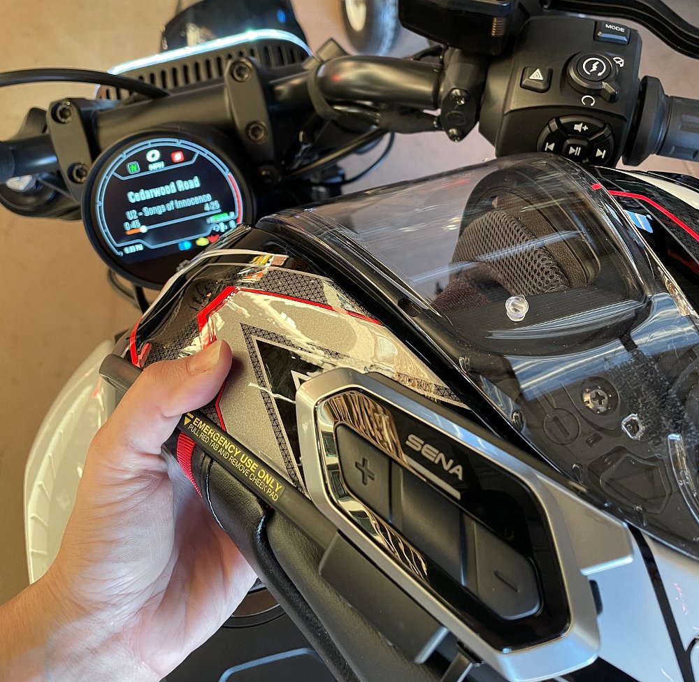 A Sena bluetooth headset on a helmet rests on the Sportster tank, while the dash shows the bike and unit are paired