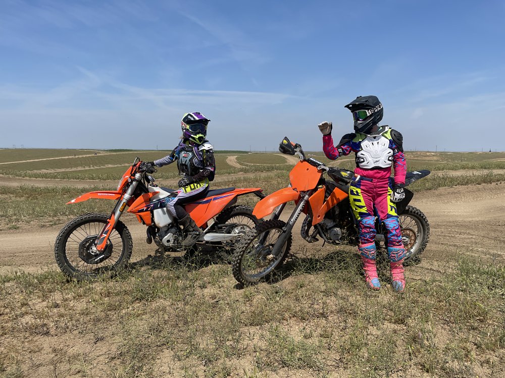 two female riders all geared up sitting on their dirtbikes