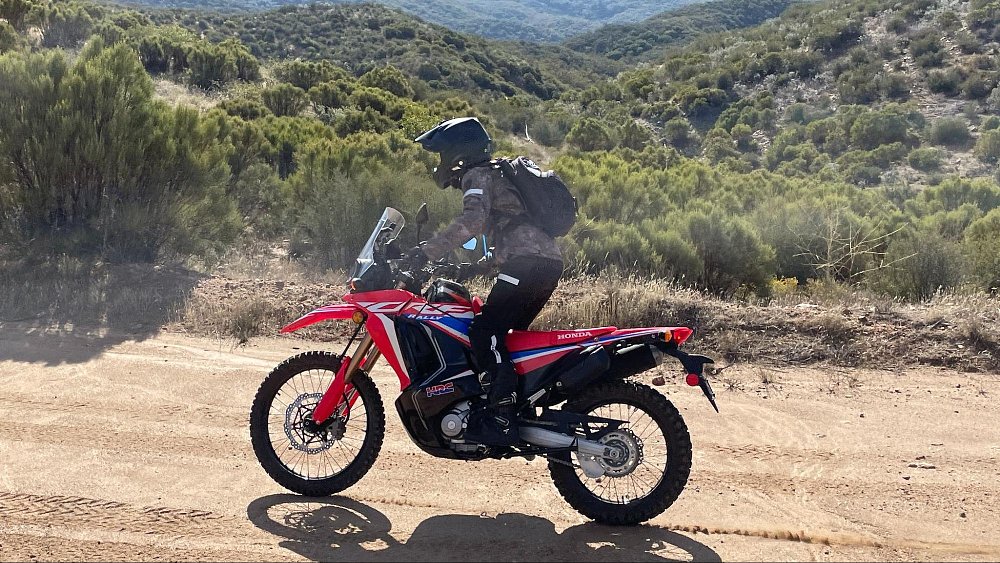 A female rider is standing up on the foot pegs while riding the Honda CRF300L Rally on a dirt trail