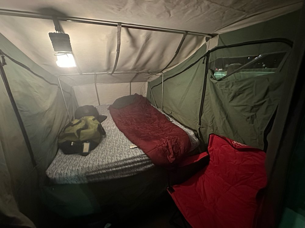 Interior image of a Kwik Kamp trailer, a mattress with a sleeping bag and a camp chair setup in the corner.