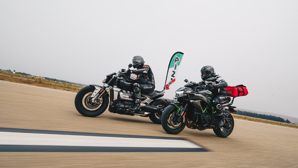 Kawasaki Z-H2 and Triumph Rocket 3 motorcycles equipped for pizza delivery riding down a straight road.