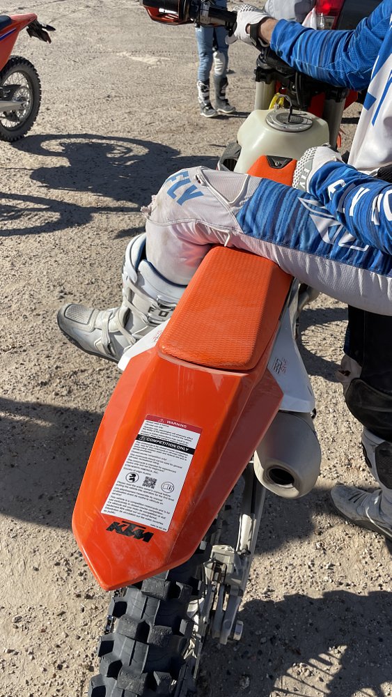 a rider is sitting on a orange ktm in the desert with a competition sticker