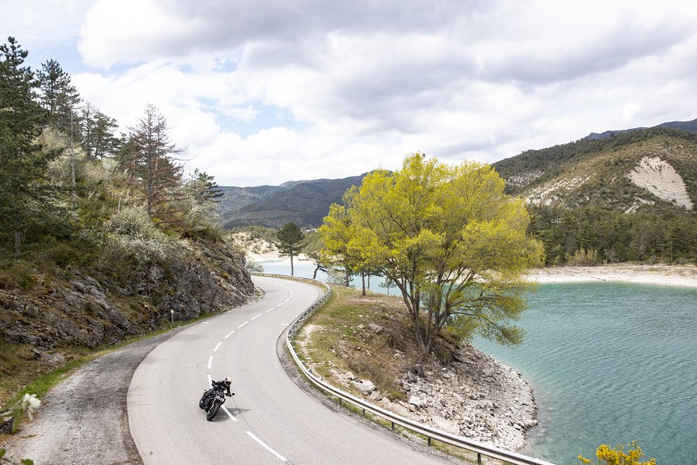 distant view of the Rocket 3 riding along a winding road beside a lake