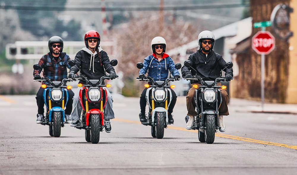 four young people riding Groms on a city street