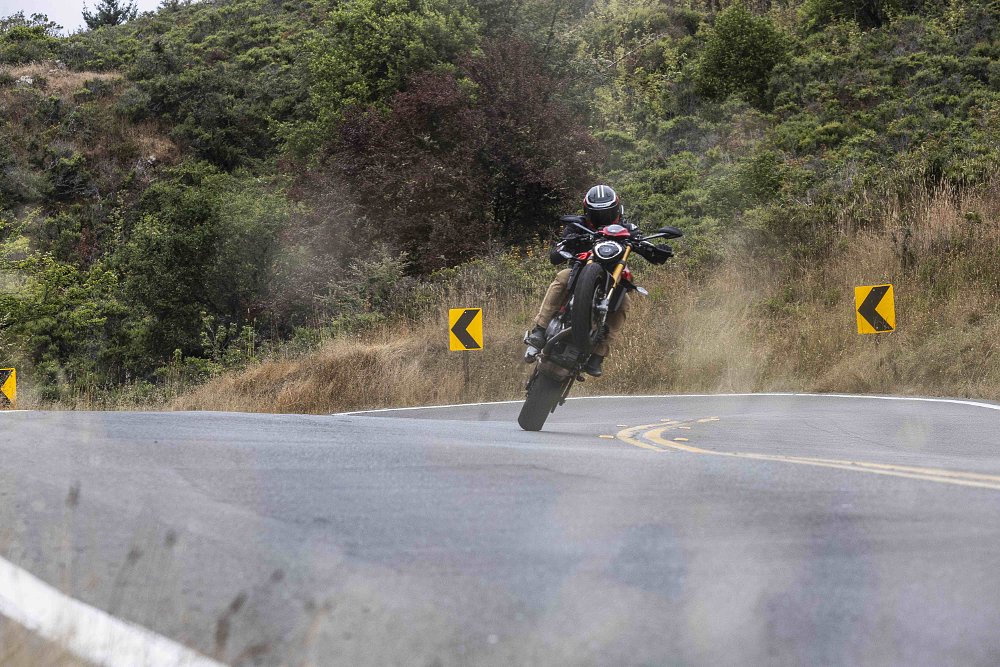 A 2024 Ducati Monster SP doing a wheelie toward camera on a twisty road.