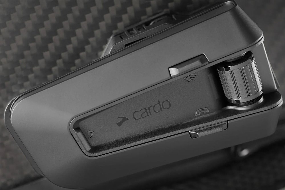 A Cardo PackTalk Pro headset mounted to the side of a carbon fiber helmet.