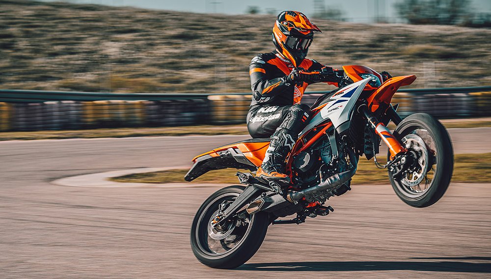 A KTM 390 SMC R rider performs a wheelie on a kart track.