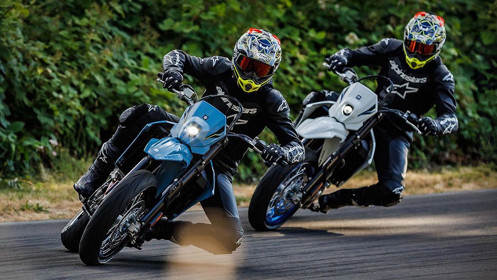 Two Suzuki DR-Z4SM riders slide their bikes into a corner.
