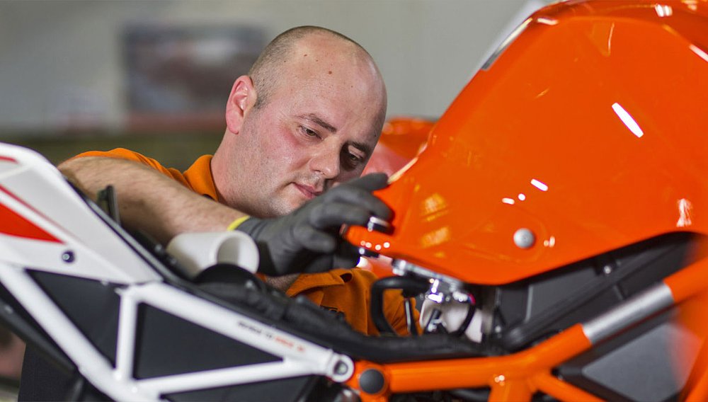 An assembly line worker mounts a gas tank on a KTM 1290 Super Duke.