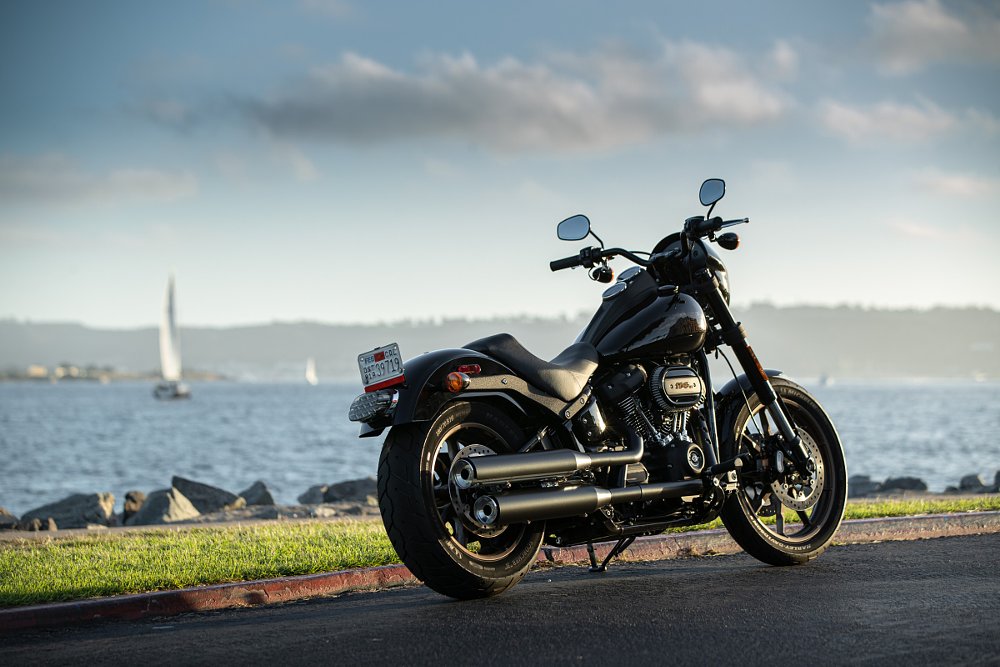 black Harley-Davidson Low Rider S parked by a lake with a sailboat in the distance