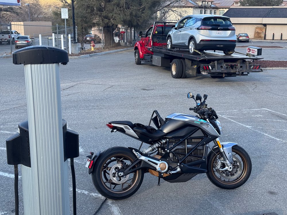 A Chevy Bolt EV arrives at a charging station on a flatbed truck while a Zero S charges in the foreground.