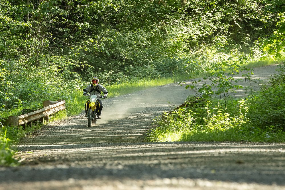 2025 Suzuki DR-Z4S riding across a bridge on a dirt road in the woods.
