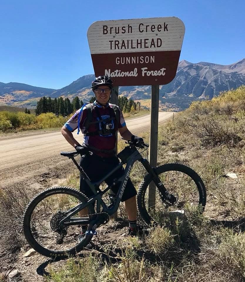 author on his bicycle in front of a sign for the Gunnison National Forest