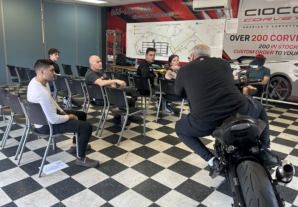 instructor demonstrates body position on a motorcycle during a classroom instructional session during the track day