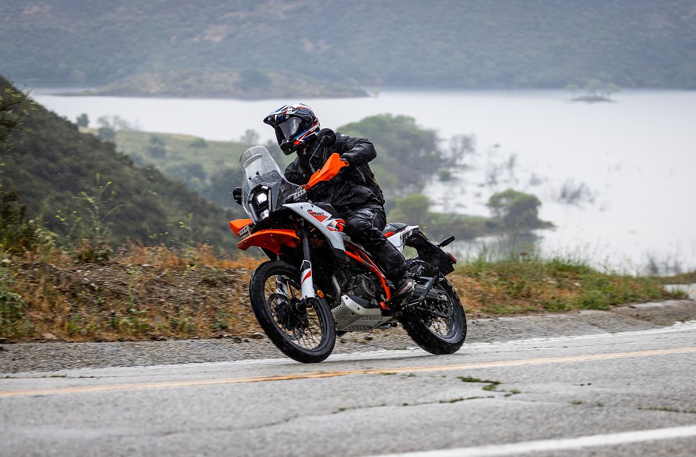 2025 KTM 390 Adventure R riding along a twisty paved road with a lake in the background.