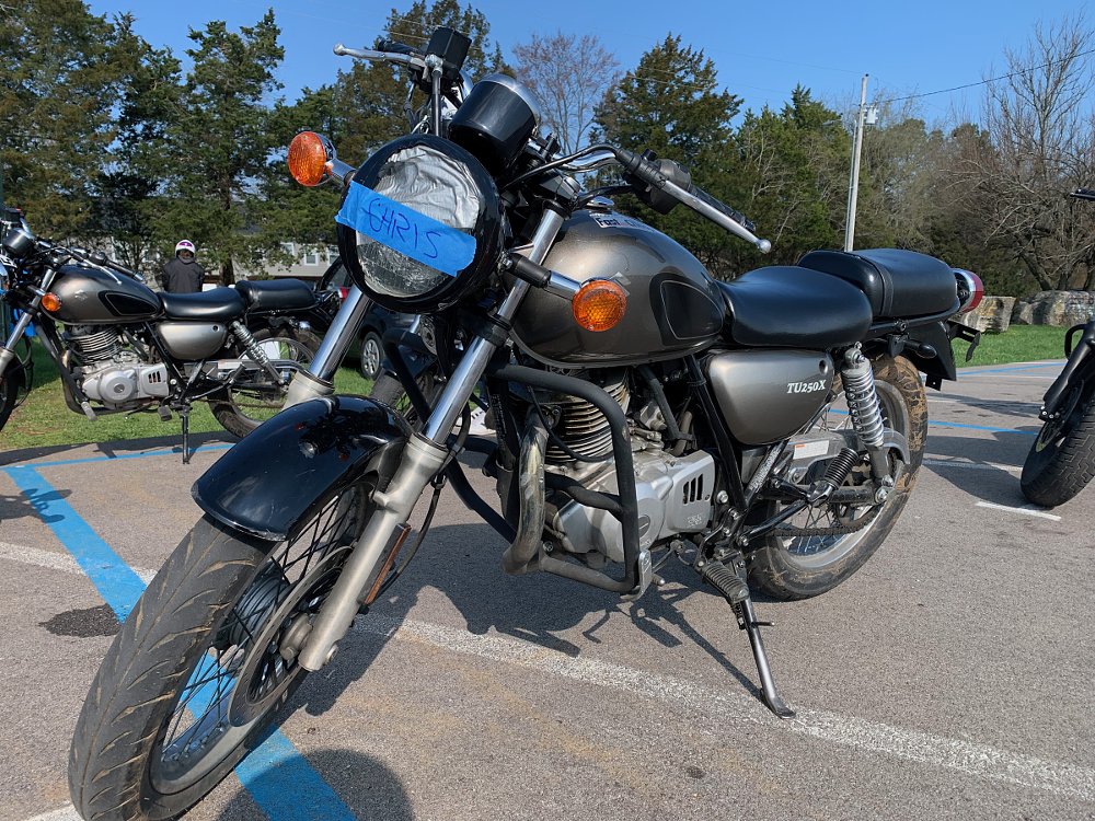 photo of a lightweight Suzuki TU250X motorcycle with tape on the headlight with the name 'Chris' written on it