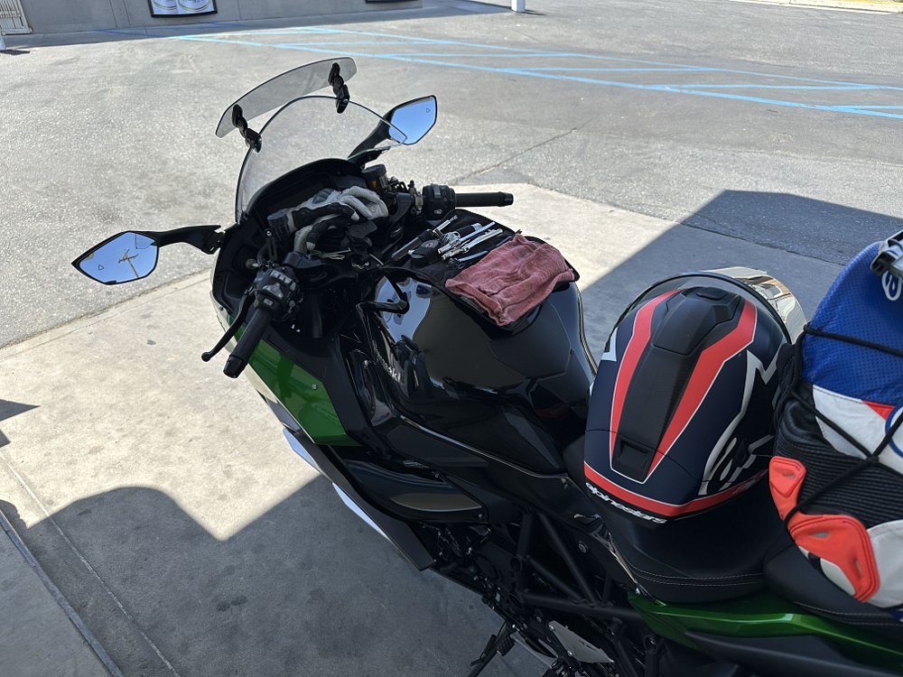 2025 Kawasaki H2 SX SE parked at a gas station with a tool kit out and an aftermarket windshield deflector being installed.