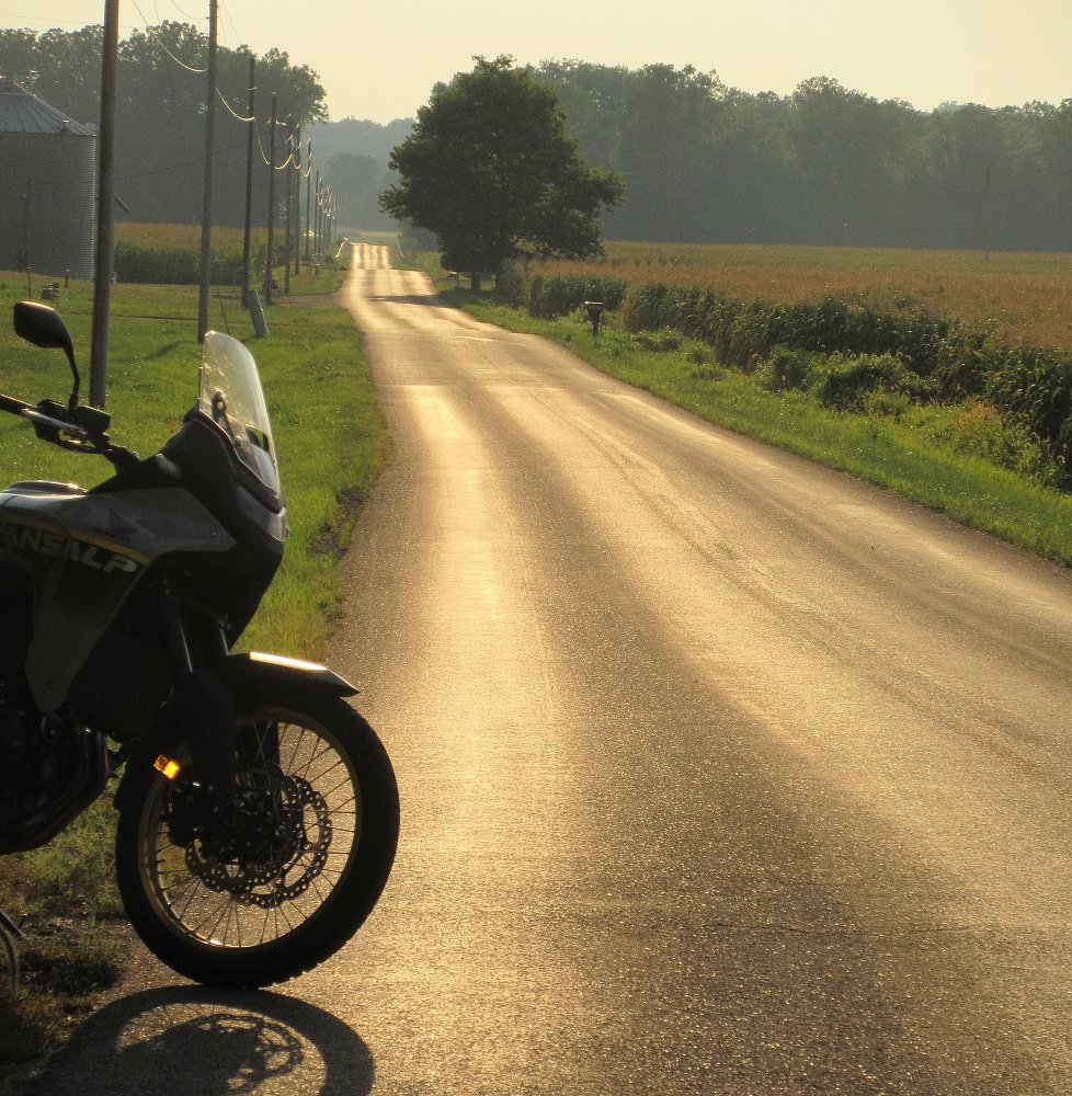 Transalp parked along a narrow country lane at sunset with the setting sun glowing on the asphalt