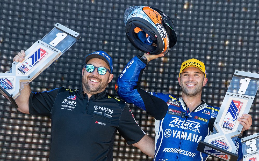 Bobby Fong smiles and holds a trophy for winning a race while a team member stands beside with another trophy